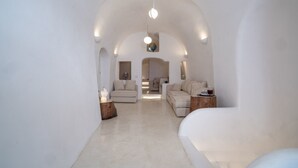 Een ruime, moderne woonkamer met een hoge gewelfde plafond, een centraal zithoek met banken, en een minimalistisch design.