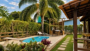 Un área de piscina con una pérgola de madera, una mesa con sillas y una variedad de plantas.