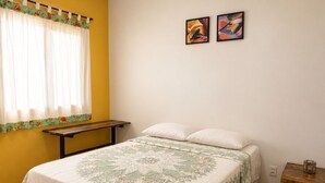 Un dormitorio con una cama, un banco de madera, una mesita de noche y dos cuadros abstractos en la pared.