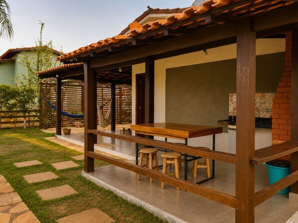 Un patio techado con una mesa y taburetes de madera, una hamaca y un muro de ladrillo.