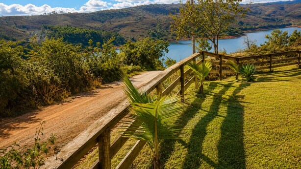 Vista panorámica de un paisaje montañoso con un sendero de tierra que lleva a una cerca de madera y una zona cubierta de césped.