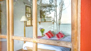 A room with a bed, a lamp, and a view of the sea through a window. - Casa Paxanax (Santa Cruz La Laguna)