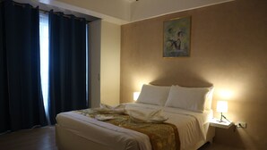 A neatly made bed with white linens and a gold throw blanket, a bedside table with a lamp, and a painting on the wall. - Hotel Casa Ilustre (Balayan)