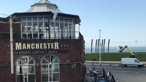 Un edificio de ladrillo con un letrero que dice "Manchester Bar" y grandes ventanales.