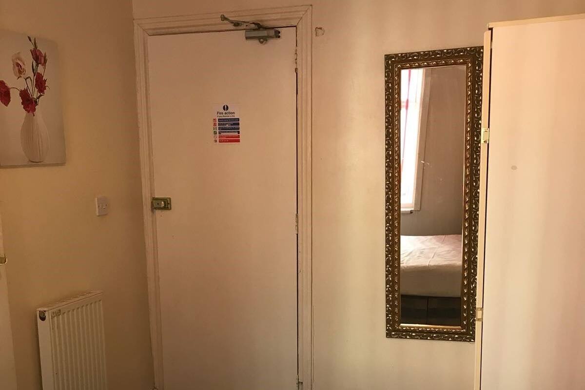 Habitación de hotel con cama, radiador, puerta con señal de emergencia contra incendios y espejo en la pared.