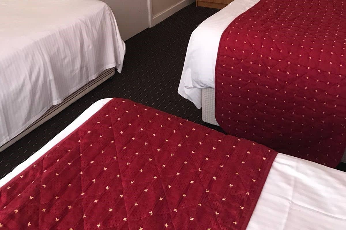 A hotel room with two beds, a wardrobe, and a radiator.