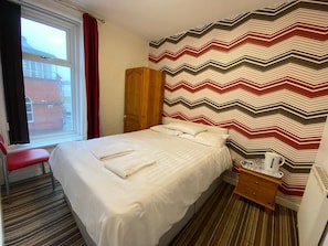 A hotel room with a bed, a chair, a nightstand, and a window. - Chilton Hotel (Blackpool)