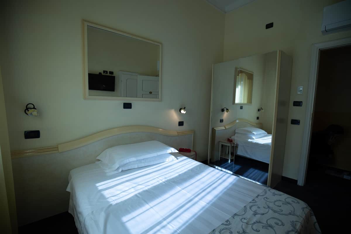 A hotel room with a large bed, a bedside table, a mirror, and a wardrobe.