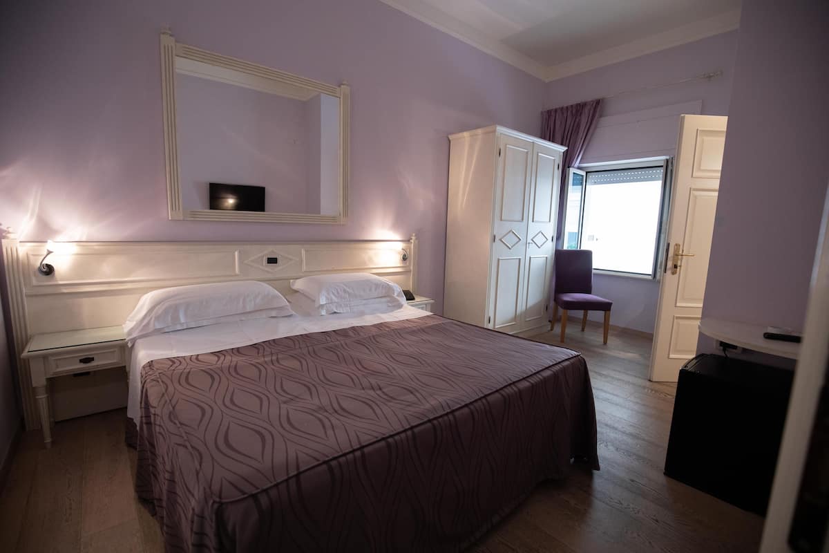 A bedroom with a large bed, a wardrobe, a chair, and a desk.