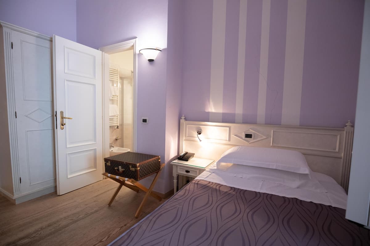 A bedroom with a bed, a nightstand, a suitcase, and a wardrobe.