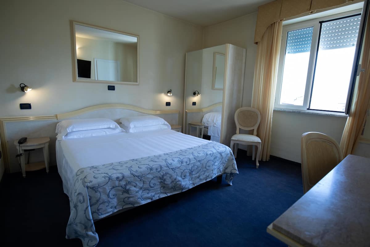 A hotel room with a large bed, two bedside tables, a chair, a desk, and a window with curtains.