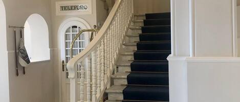 A grand staircase with white balusters and dark blue carpeted steps leading to a landing.