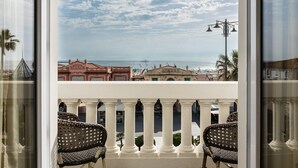 Un balcon avec des fauteuils en osier, une vue sur la mer et des bâtiments en arrière-plan.