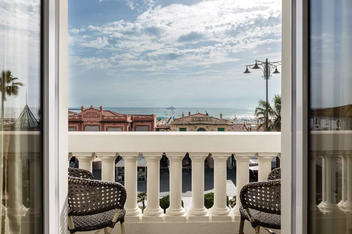 A balcony with wicker chairs, a view of the sea, and buildings in the background.
