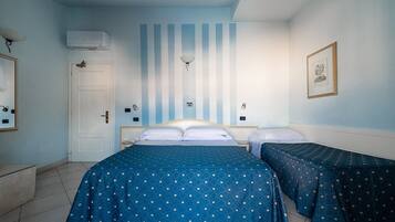 A room with a large bed, two smaller beds, a door, an air conditioning unit, a wall-mounted light, and a framed picture.