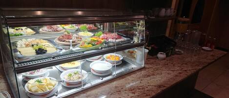 Buffet com diversos alimentos e uma vitrine de vidro.