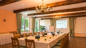 A conference room with a long table, chairs, a chandelier, and a projector screen. - Hotel Knorre (Meissen)