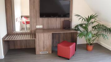 Una habitación moderna con un escritorio de madera, un televisor de pantalla plana, un taburete rojo y una planta en maceta.