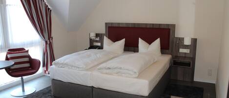 Camera moderna con un letto grande, una poltrona rossa, comodini e una finestra con tende.