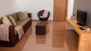 A living room with a sofa, a chair, a wooden desk with a TV, and a door.