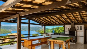 A pool table and a billiards table in a room with large windows overlooking a lake and hills.