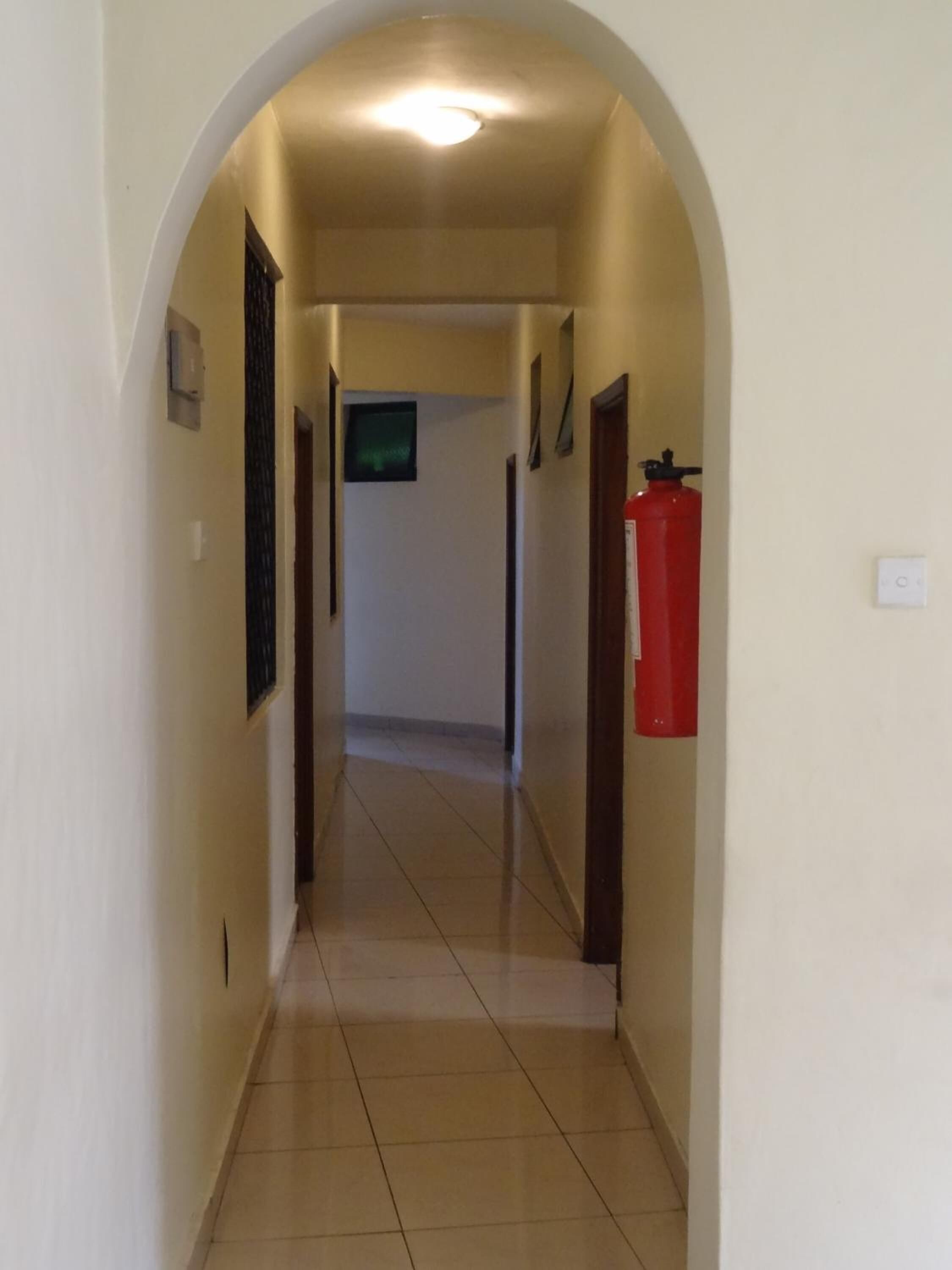 Um corredor com teto em arco, um extintor de incêndio fixado na parede e uma porta no final.
