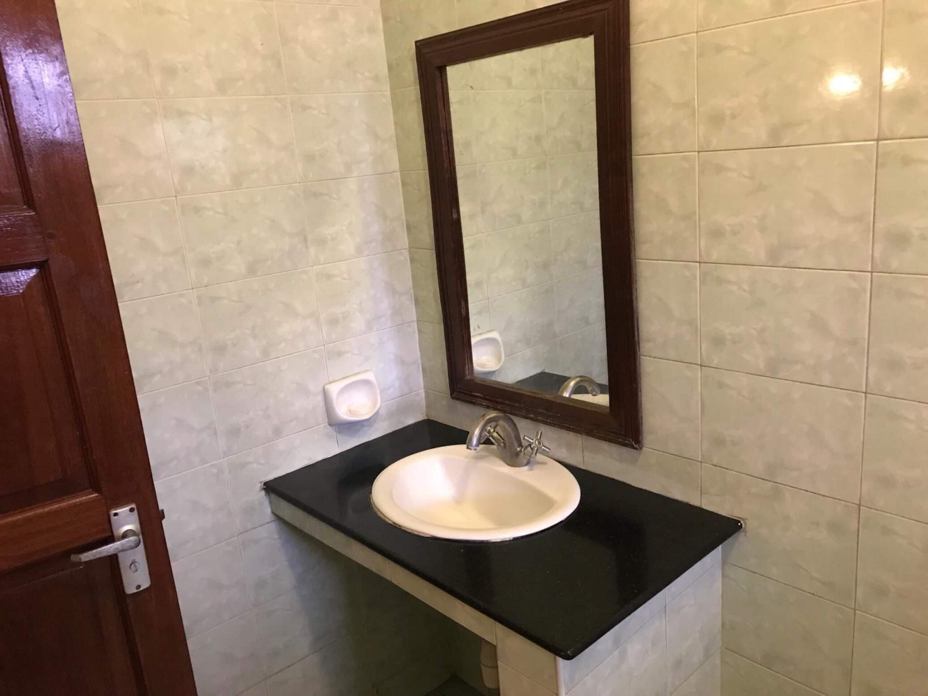 A bathroom with a white sink, black countertop, and a mirror with a wooden frame.