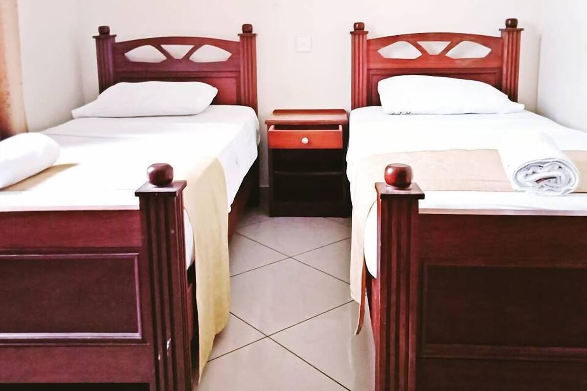 Two wooden beds with white linens, a small bedside table, and a wall-mounted light fixture.