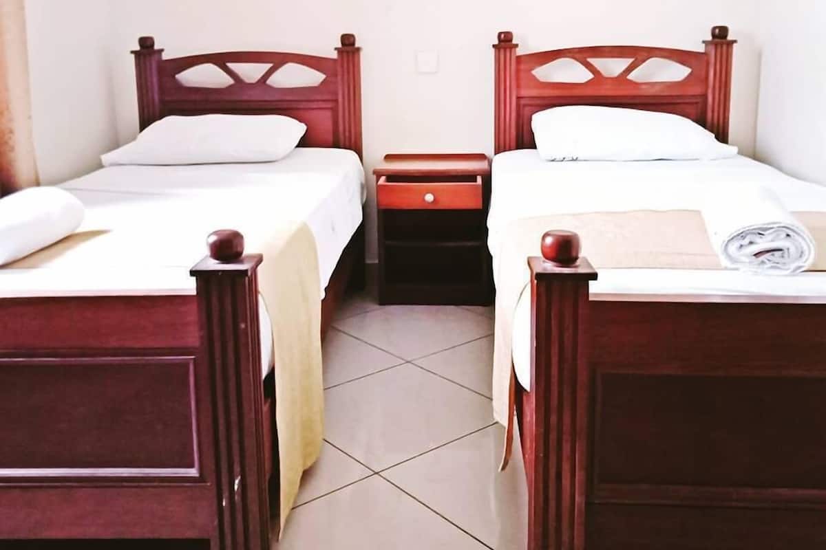 Two wooden beds with white linens, a small bedside table, and a wall-mounted light fixture.