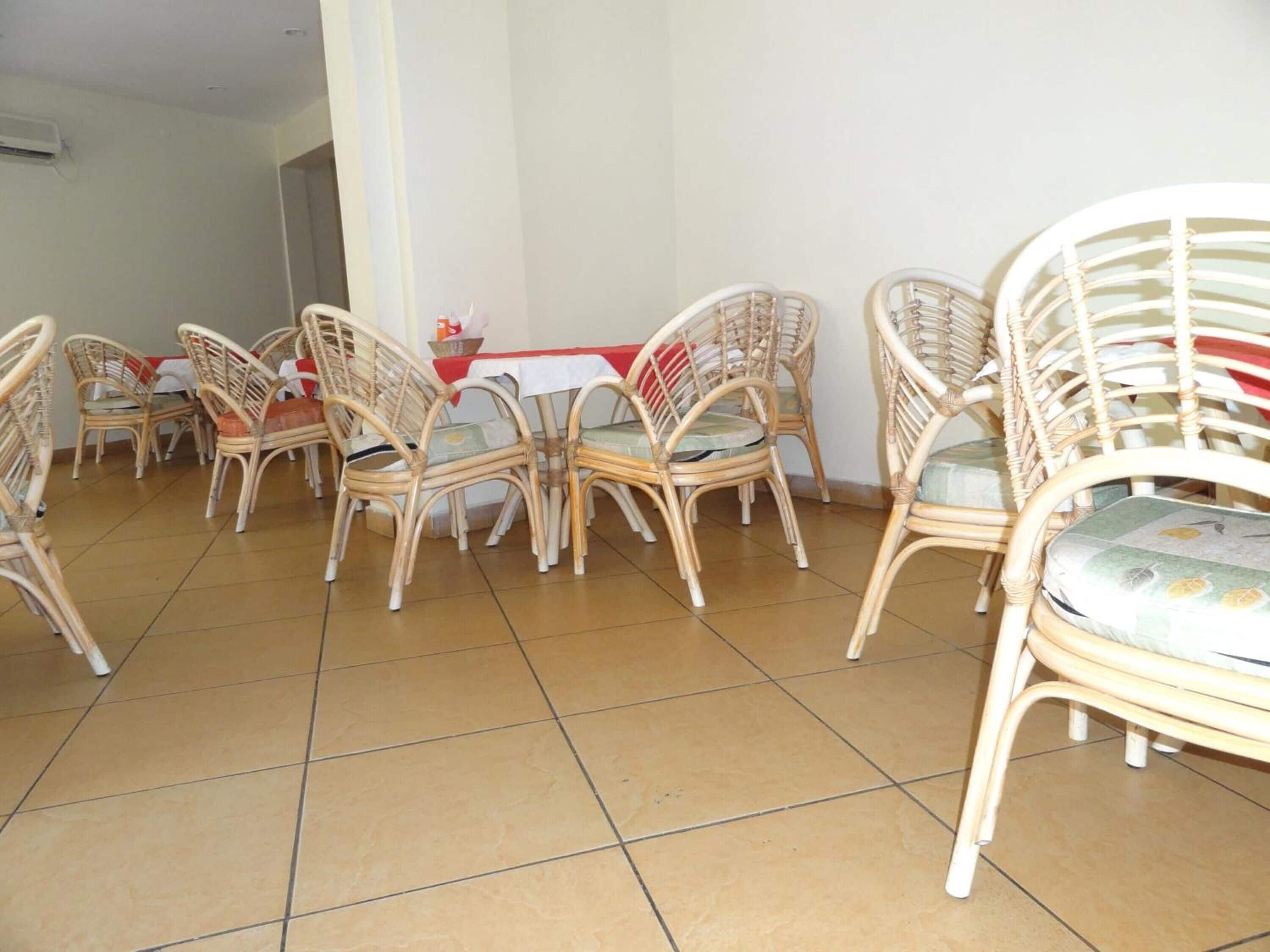 Comedor con sillas de mimbre y una mesa, suelo de baldosas y pared blanca.