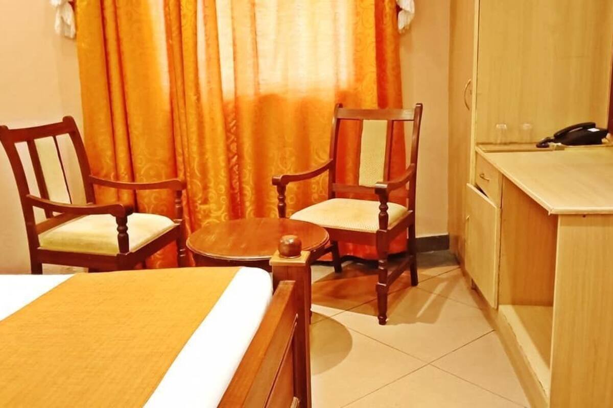A hotel room with a bed, two wooden chairs, a small round table, a wooden desk, and a telephone.