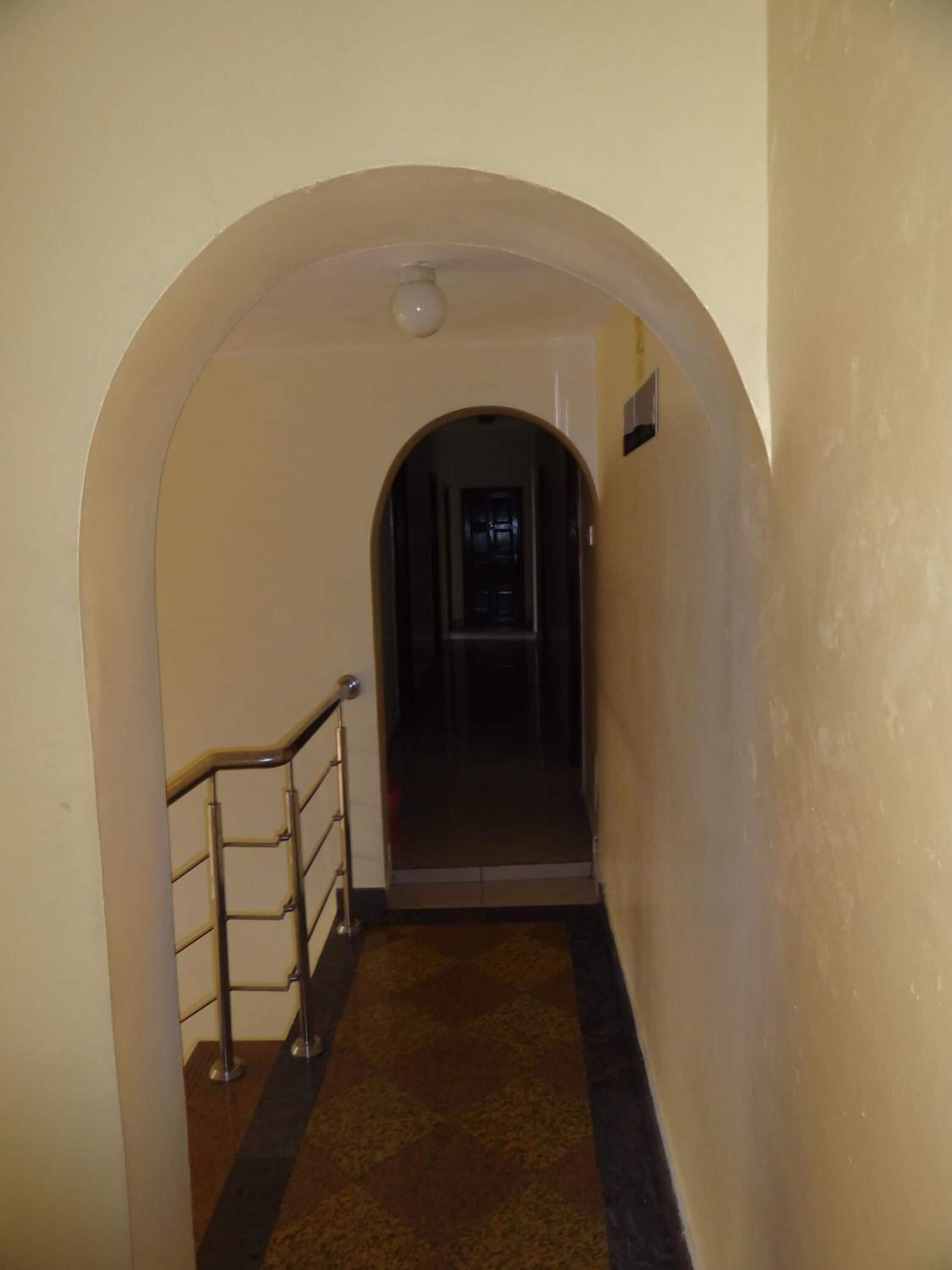 A narrow hallway with a metal railing on one side, leading to a dark doorway at the end.