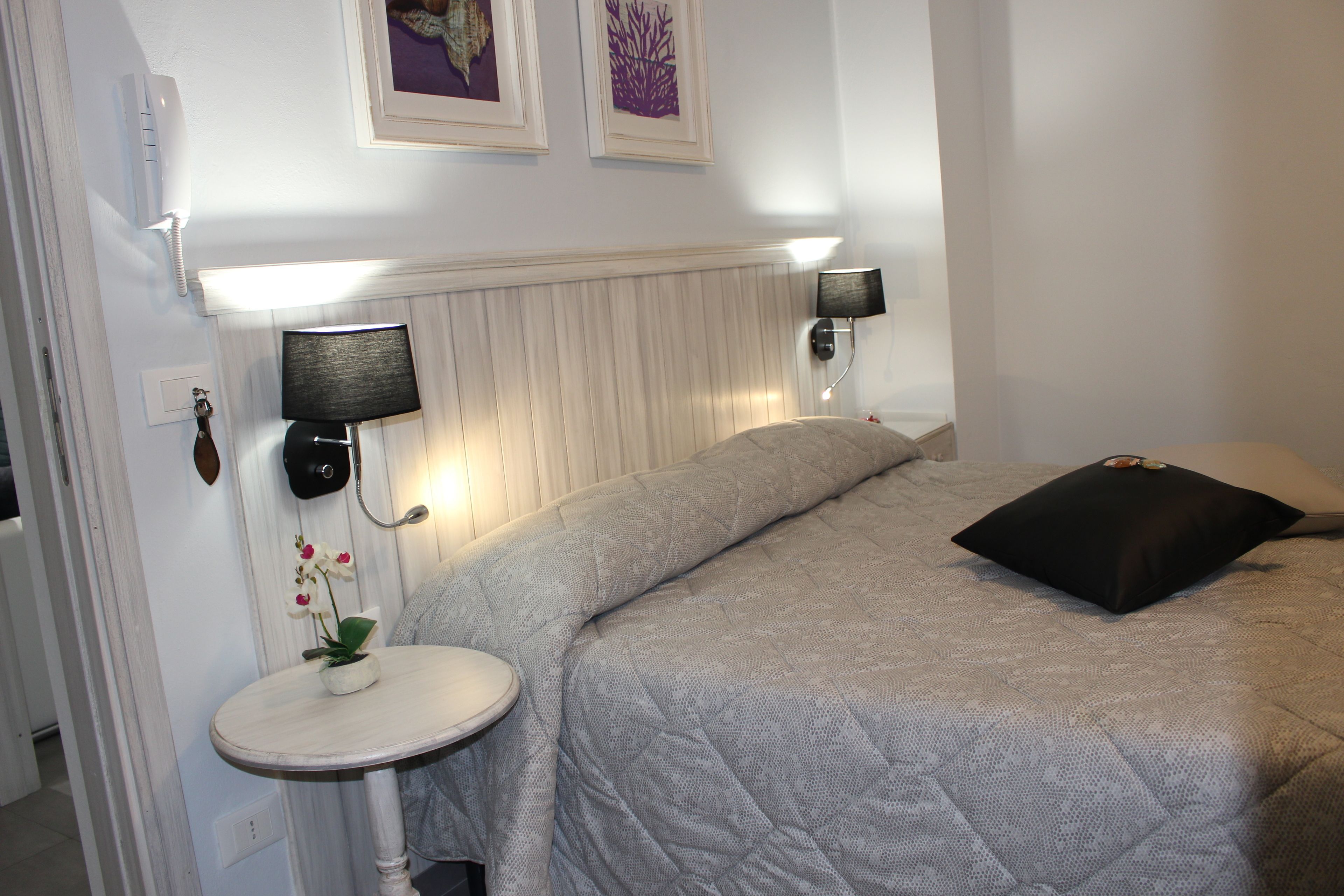 A bedroom with a bed, bedside lamps, a small table with a plant, and a wall-mounted telephone.
