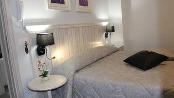 A bedroom with a bed, bedside lamps, a small table with a plant, and a wall-mounted telephone.
