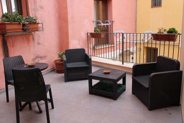 A balcony with wicker furniture, potted plants, and a metal railing.