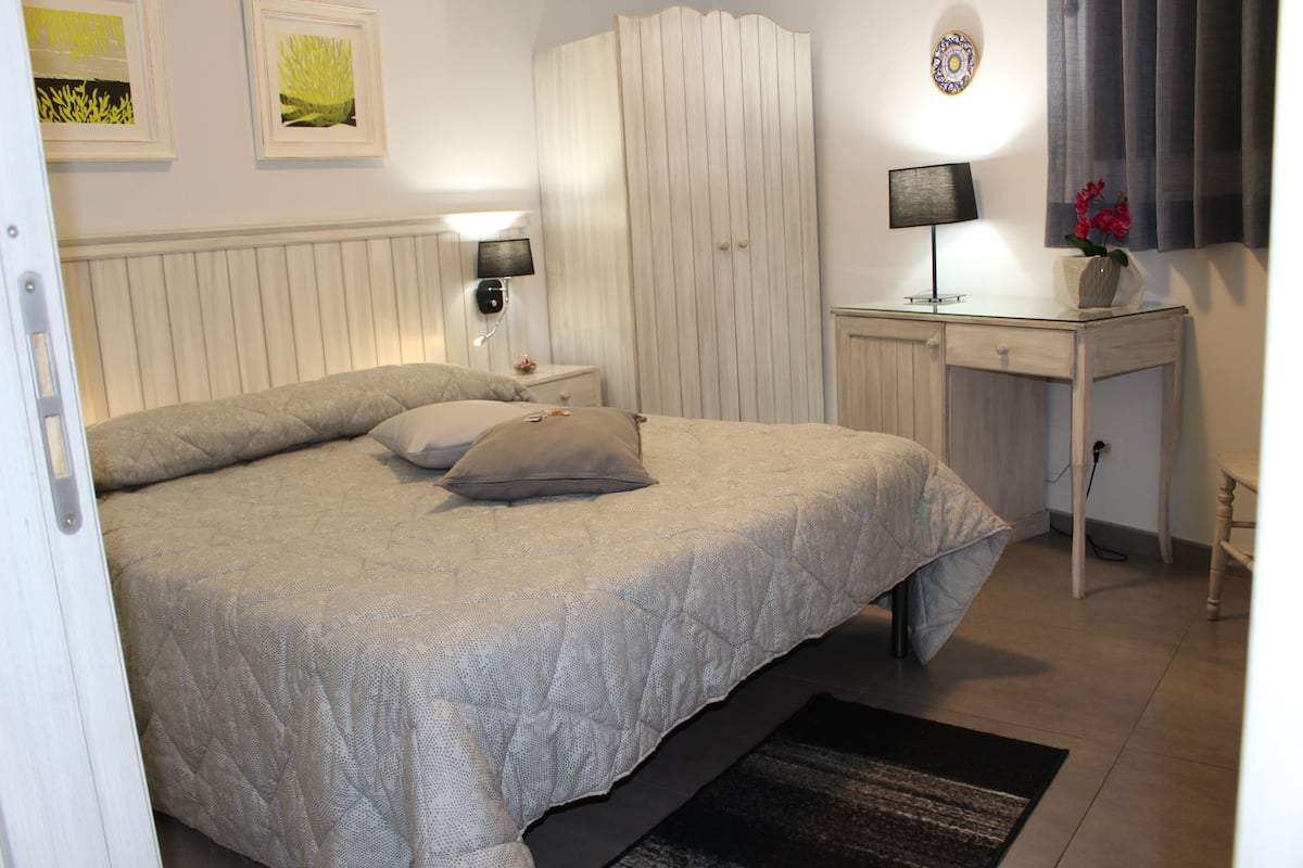 A bedroom with a bed, bedside tables, a desk, and a chair.