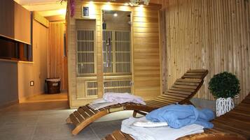 A sauna room with two wooden loungers, a small trash bin, and a potted plant.