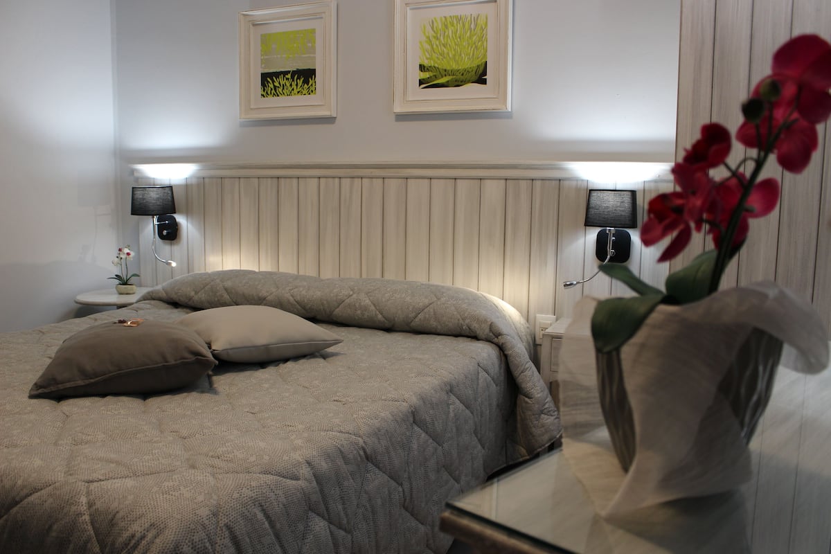 A neatly made bed with a quilted blanket and pillows, a bedside table with a lamp, and two framed pictures on the wall.