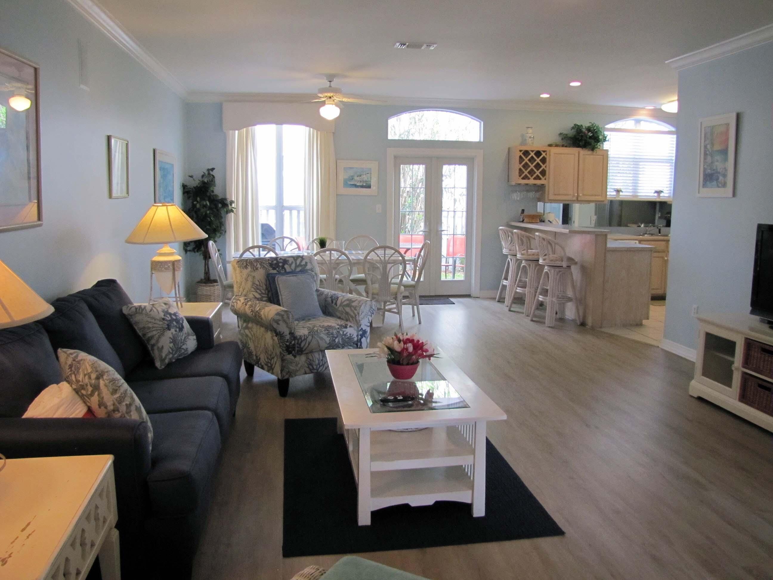 A living room with a sofa, armchair, and coffee table, a dining area with chairs, and a kitchen with bar stools.