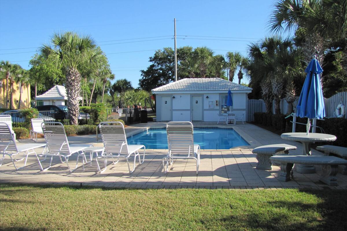 A swimming pool area with lounge chairs, a small table, and a covered seating area.