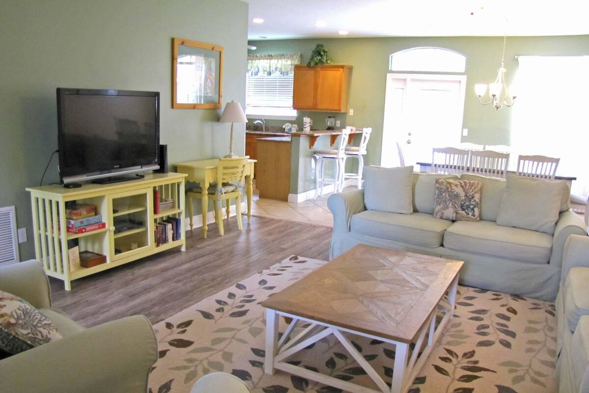 A living room with a TV, a sofa, a coffee table, and a dining area with chairs and a table.