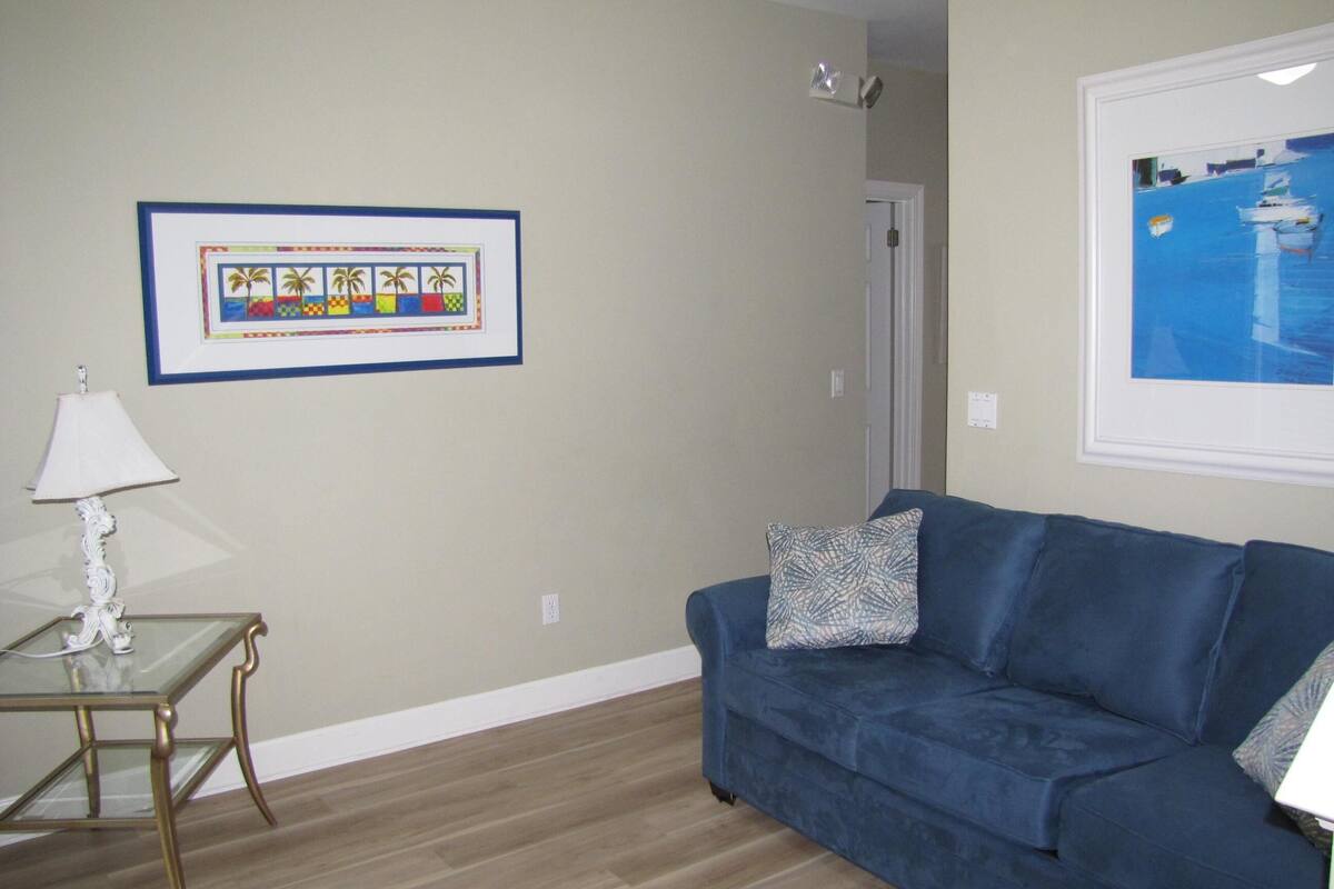 A living room with a blue sofa, a glass coffee table, a framed picture, and a lamp.