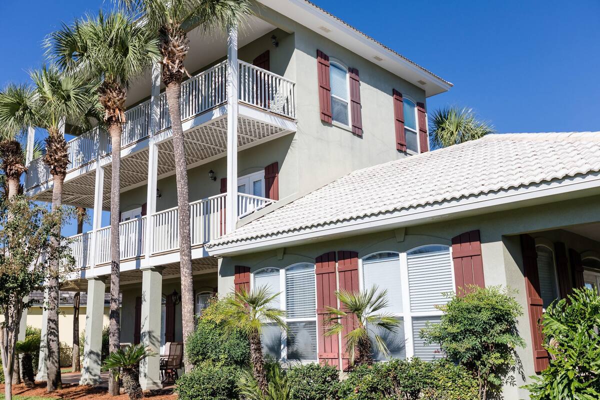 A multi-story building with balconies, red shutters, and palm trees.