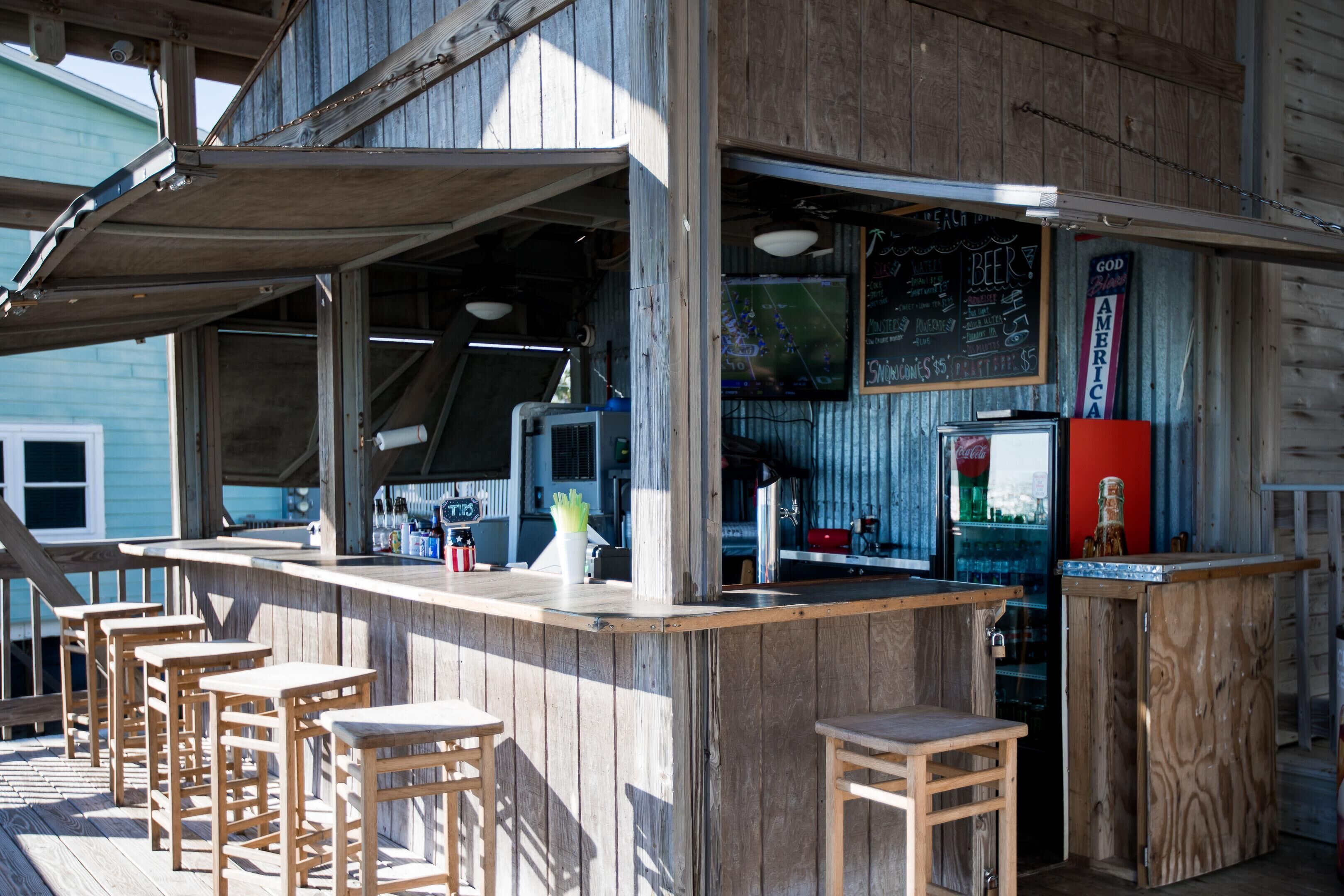 A wooden bar area with stools, a counter, and a refrigerator.