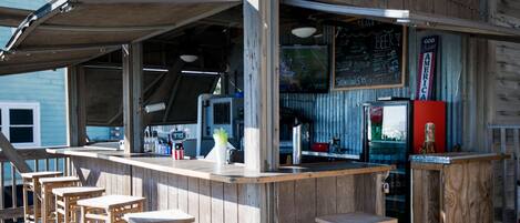 A wooden bar area with stools, a counter, and a refrigerator.