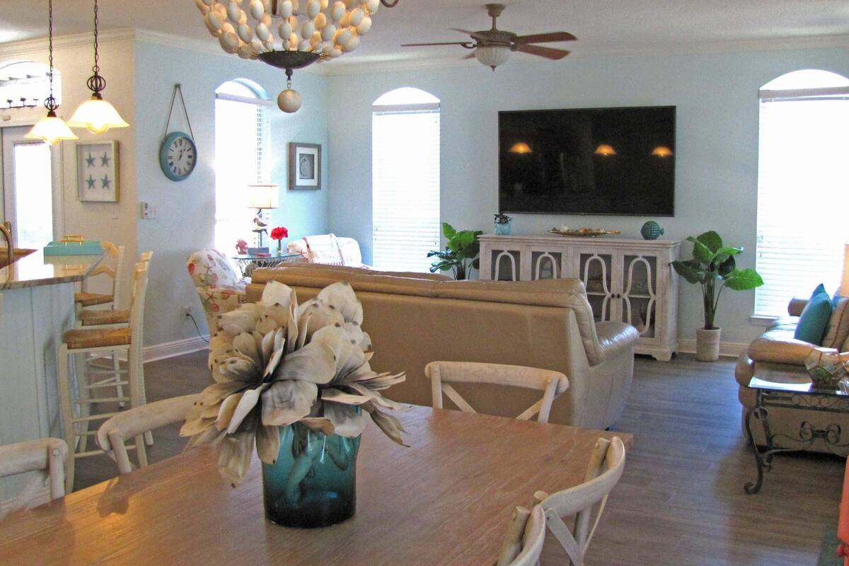 A spacious living room with a wooden dining table, a sofa, and a television mounted on the wall.