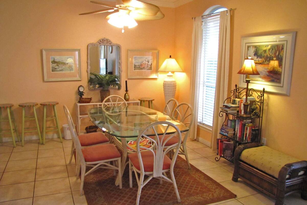 A dining area with a glass-top table, wicker chairs, and a red rug.