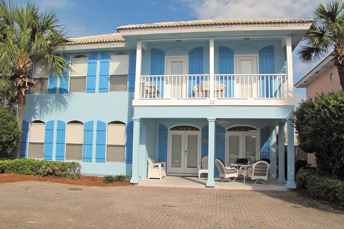 A two-story building with a balcony, numbered 23, featuring a covered patio with outdoor furniture.