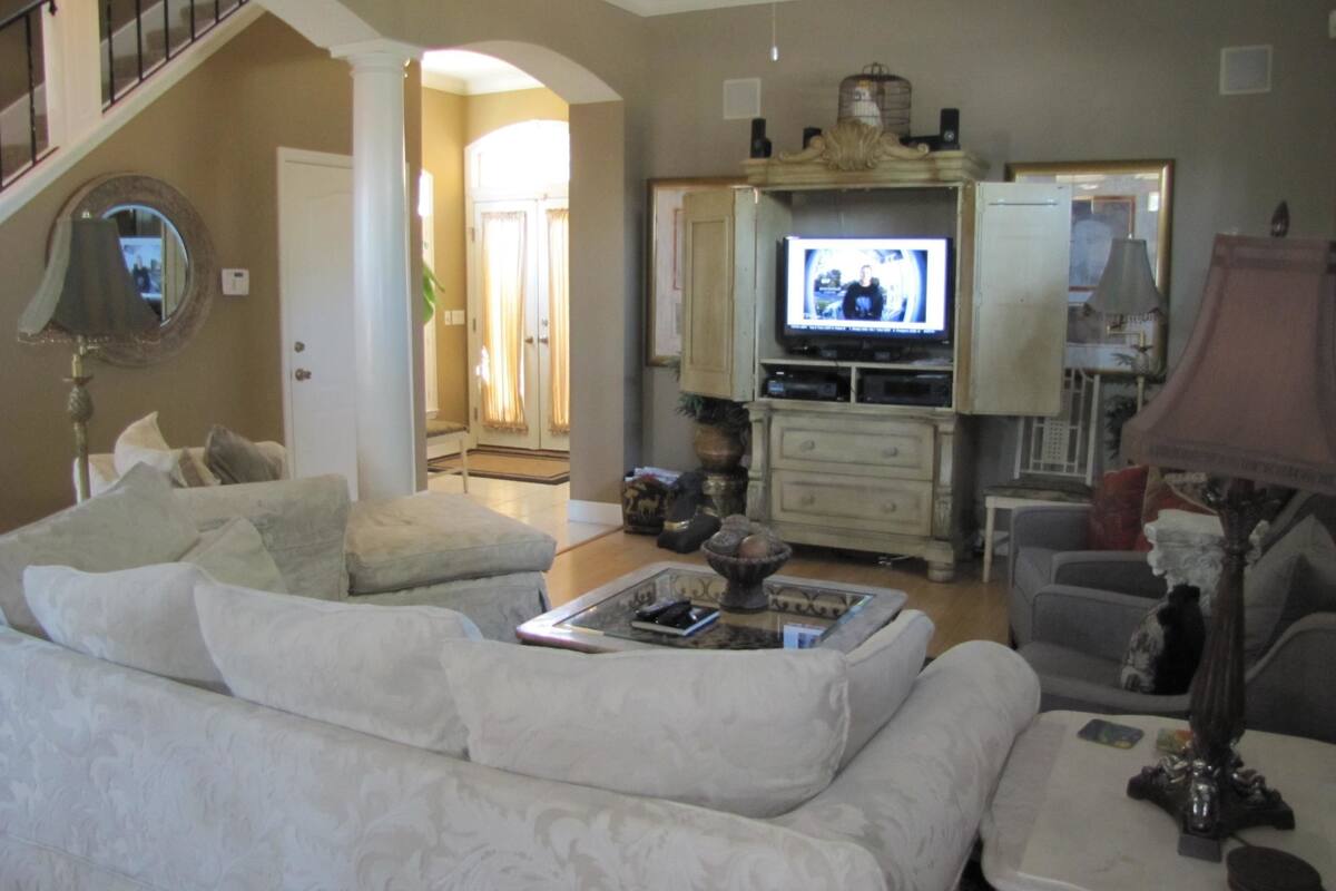 A living room with a sofa, a coffee table, a television, and a lamp. There is a staircase in the background.