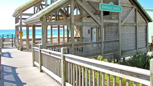 Ein Holzsteg führt zu einem Strandhaus namens 'Emerald Shores' mit einer Veranda und Blick auf den Ozean.